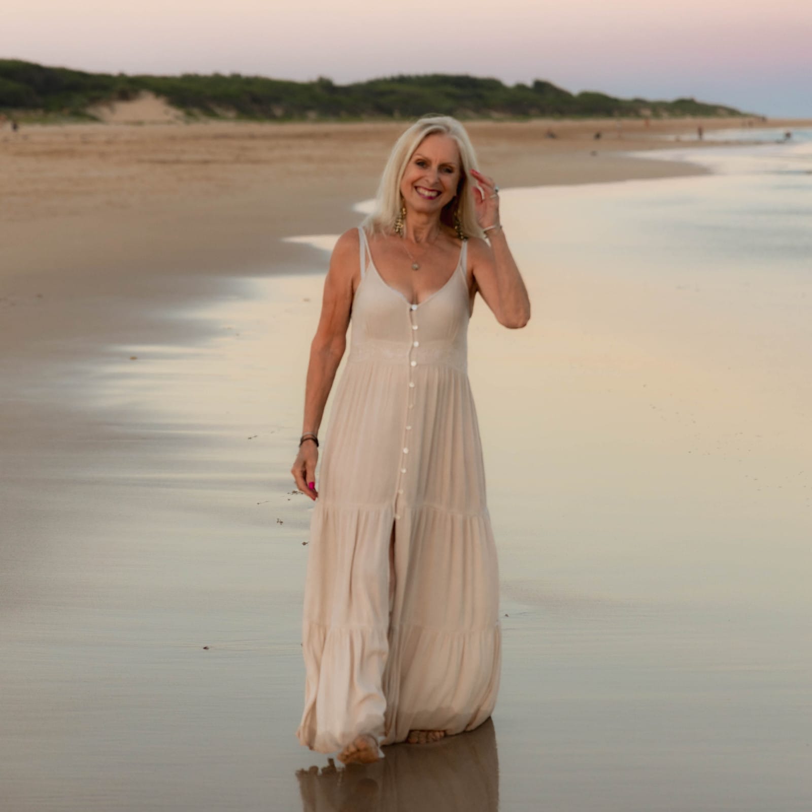 A serene moment captured as Val Hood, an Evidential Medium, walks along the beach in a beautiful long dress, embracing nature.