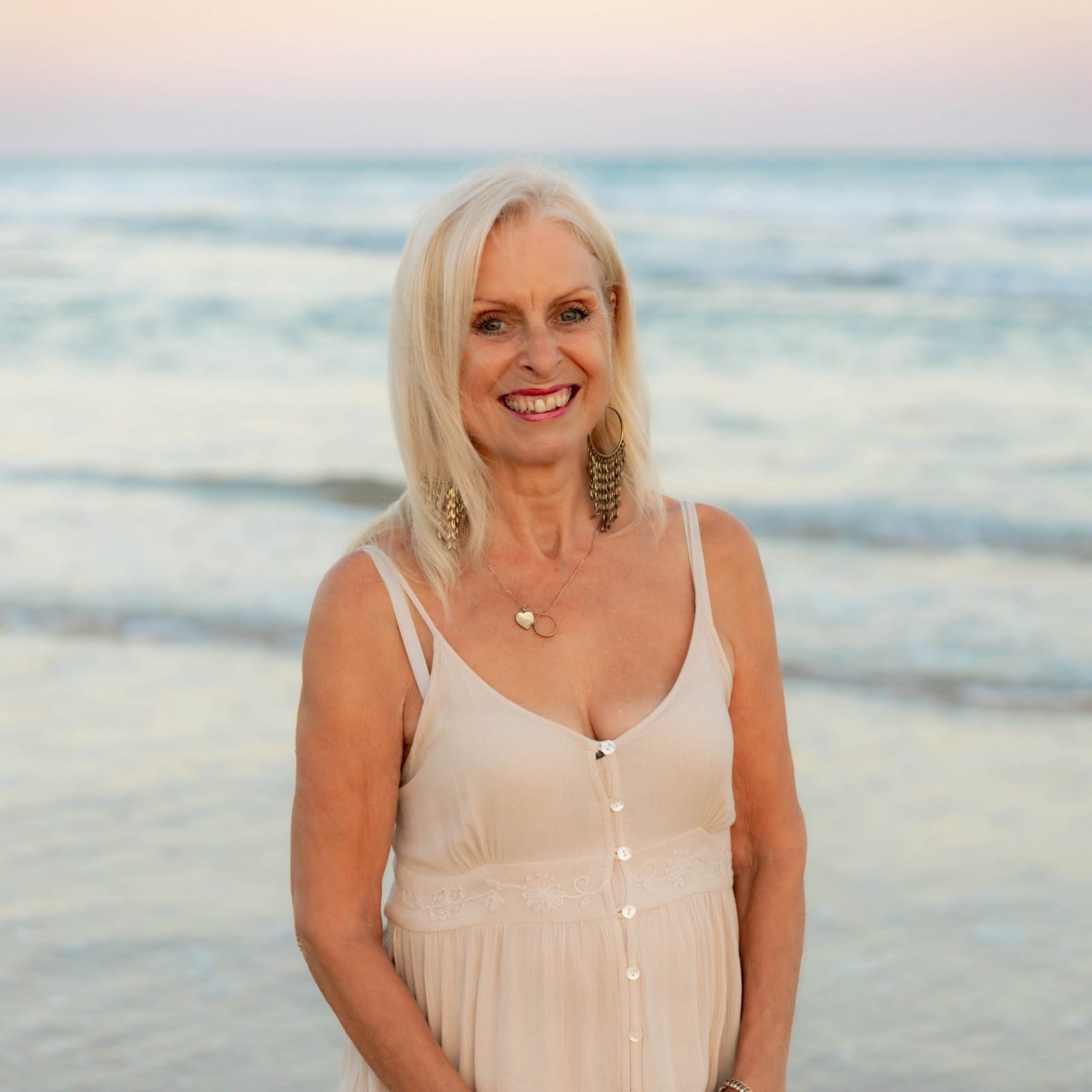 On the beach, Val Hood, a blonde-haired Evidential Medium, embraces the beauty of the ocean and the warmth of the sun.